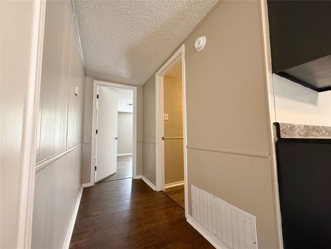 Hallway featuring dark wood-type flooring, baseboards, a textured ceiling, and visible vents | Image 8