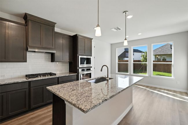 Kitchen with stainless steel appliances, tasteful backsplash, under cabinet range hood, light wood-style flooring, and dark brown cabinets | Image 5