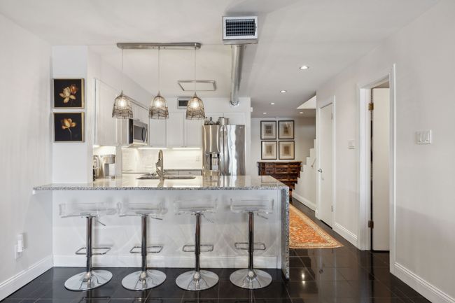 Open kitchen with bar seating facing entryway/foyer with half bath on the right. | Image 11