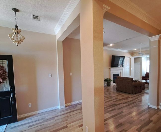 Entrance foyer with wood finished floors, a fireplace, a chandelier, ornamental molding, and baseboards | Image 4