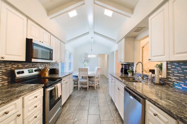 Kitchen featuring stainless steel appliances, tasteful backsplash, white cabinetry, light marble finish floors, and dark stone countertops | Image 11