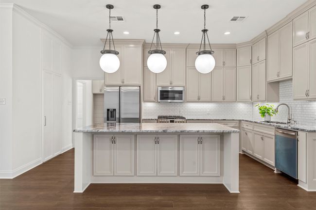 Kitchen featuring stainless steel appliances, a kitchen island, decorative backsplash, dark wood-type flooring, and light stone countertops | Image 11