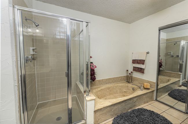 Bathroom with a bath, a textured ceiling, tile patterned flooring, and a stall shower | Image 10