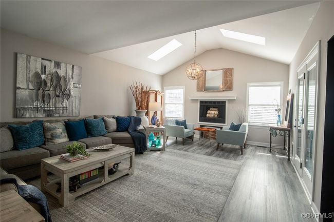 Living room featuring vaulted ceiling with skylight, baseboards, an inviting chandelier, and wood finished floors | Image 8