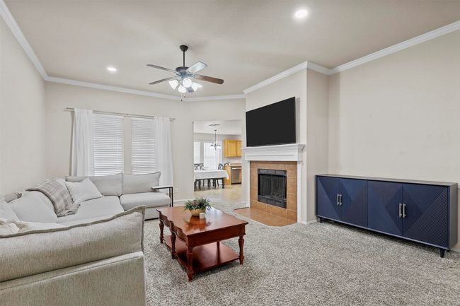 Living area with a tile fireplace, ceiling fan, carpet flooring, crown molding, and recessed lighting | Image 6