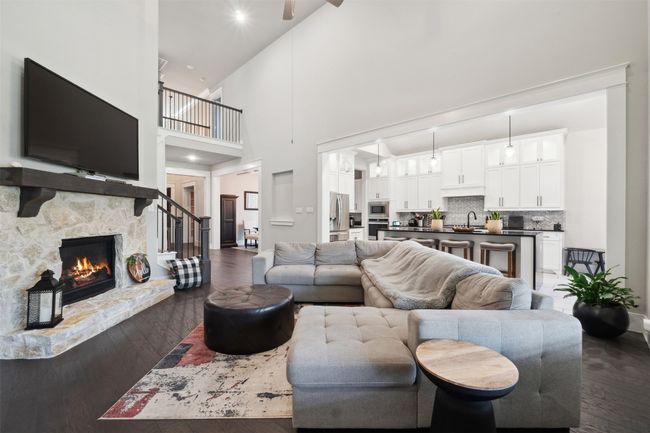 Living room with dark wood-type flooring, a towering ceiling, a stone fireplace, and a ceiling fan | Image 11
