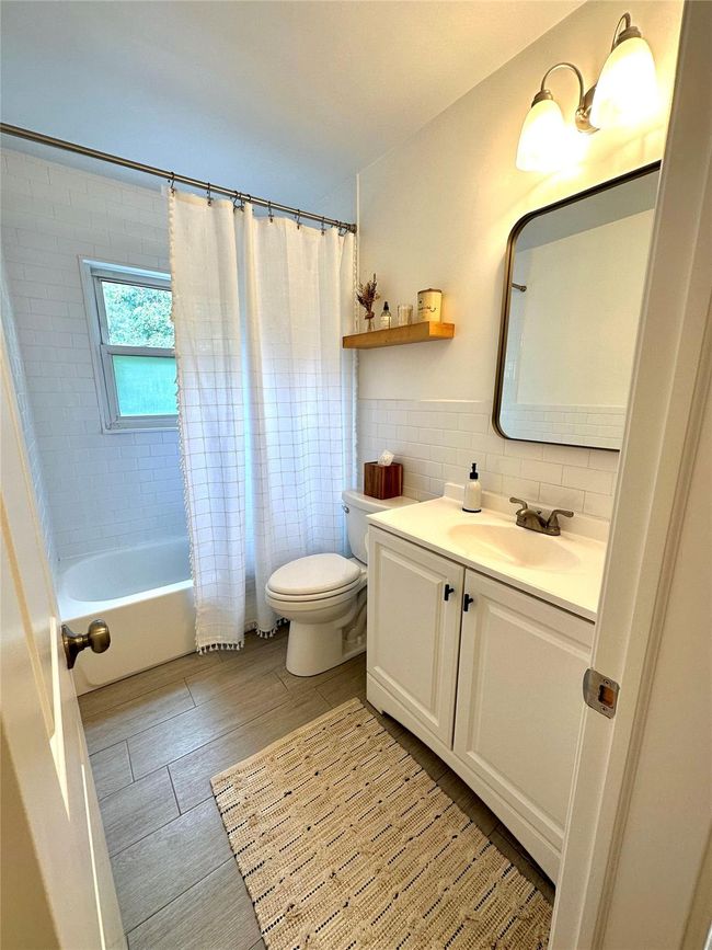 Full bath featuring toilet, tile walls, vanity, shower / bath combination with curtain, and wood finished floors | Image 13