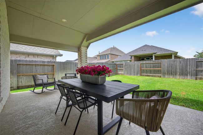Covered back patio with extended roofline provides shaded outdoor space for dining or relaxing. Enjoy a fully fenced yard with lush green grass and plenty of privacy. | Image 29