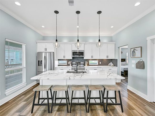 Stylish island kitchen with stunning quartz countertops, pendant & recessed lighting, stainless appliances, a herringbone tile backsplash, and bartop seating for six—designed to impress and fully equipped for coastal entertaining. | Image 14