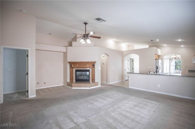 Unfurnished living room featuring visible vents, light carpet, a high end fireplace, arched walkways, and ceiling fan with notable chandelier | Image 15