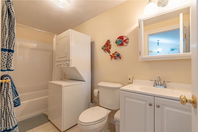 Bathroom featuring estacked washer and dryer, vanity, shower / tub combo with curtain, and tile patterned floors | Image 11