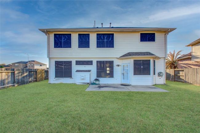 This photo shows the rear view of a two-story house with a spacious, fenced backyard. The exterior is light-colored with multiple windows and a small concrete patio, offering a great space for outdoor activities. | Image 6