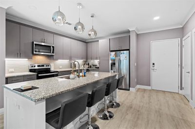 Kitchen featuring backsplash, appliances with stainless steel finishes, light stone counters, and light hardwood / wood-style floors | Image 1