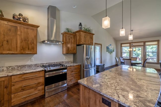 Kitchen with stainless steel appliances, island exhaust hood, brown cabinetry, dark wood-type flooring, and high vaulted ceiling | Image 14