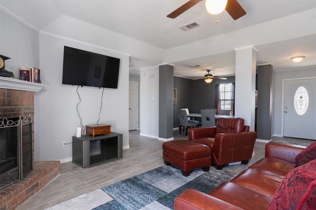 Living room featuring a ceiling fan, a brick fireplace, baseboards, wood tiled floors, and crown molding | Image 6