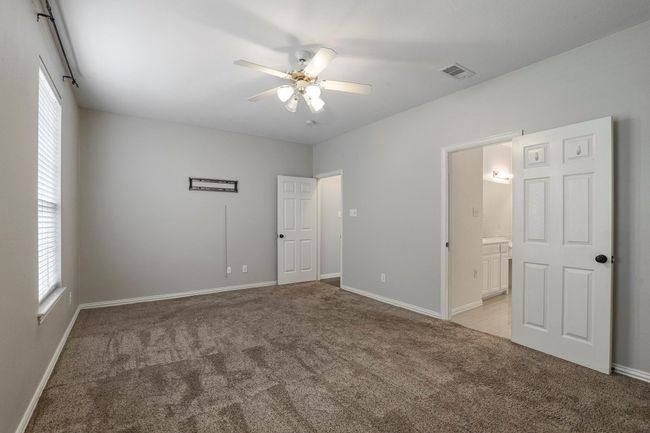 Unfurnished bedroom with light carpet, multiple windows, connected bathroom, and ceiling fan | Image 10