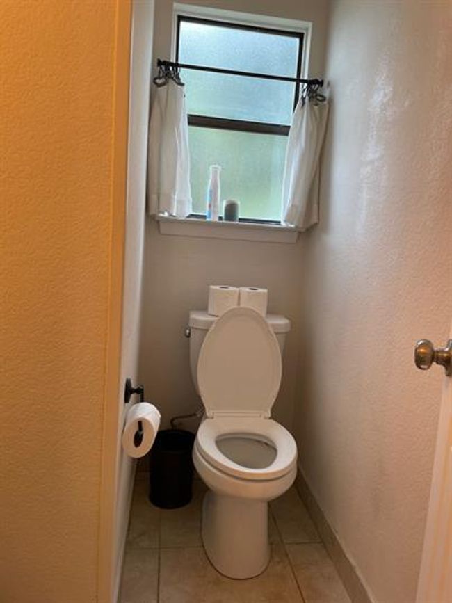 Bathroom with toilet, a textured wall, tile patterned floors, and baseboards | Image 12