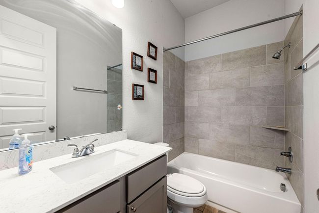 Secondary bathroom features light countertops and dark cabinets, neutral paint, shower/tub combo with tile surround, large mirror, tile floors and plenty of space to accommodate any visiting family or guests. | Image 16
