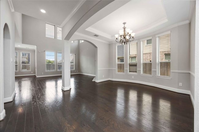 This spacious, open-concept living area features rich hardwood floors, large windows for natural light, and elegant archways. The room is accented by a stylish chandelier and high ceilings. | Image 10