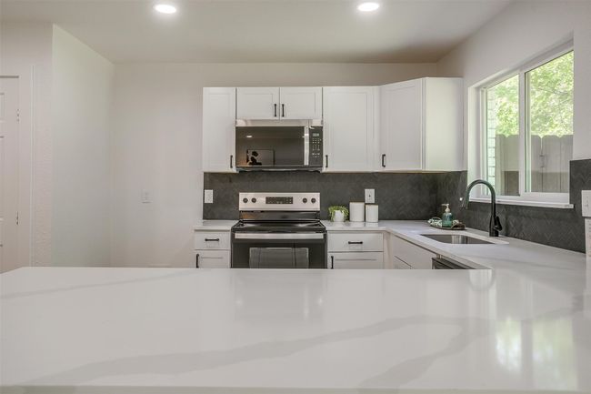 Kitchen with stainless steel appliances, decorative backsplash, light countertops, white cabinets, and recessed lighting | Image 14