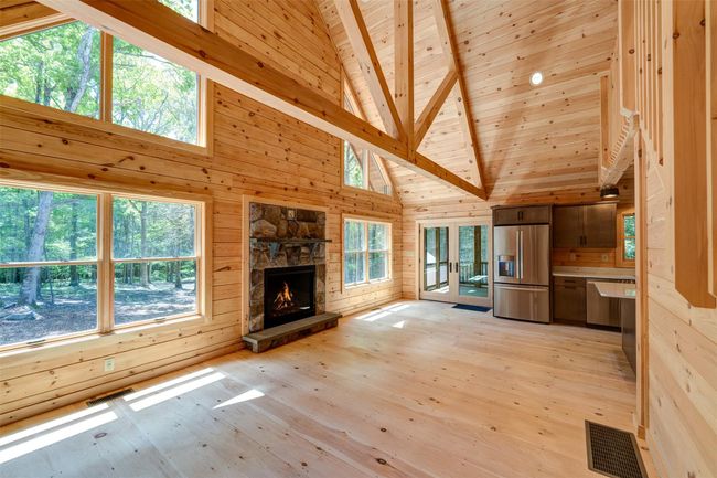 Unfurnished living room with high vaulted ceiling, wood walls, wooden ceiling with exposed beams, light wood finished floors, and a stone fireplace | Image 7
