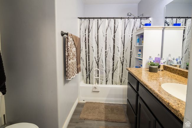 Bathroom with toilet, baseboards, shower / bath combo with shower curtain, wood finished floors, and vanity | Image 17