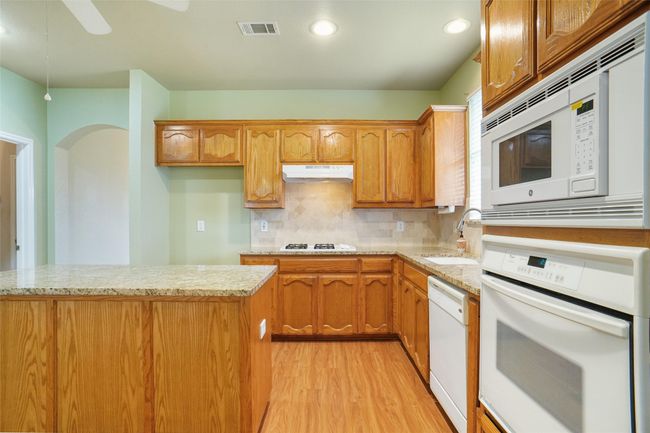Kitchen with a sink, light wood-type flooring, under cabinet range hood, white appliances, and visible vents | Image 8