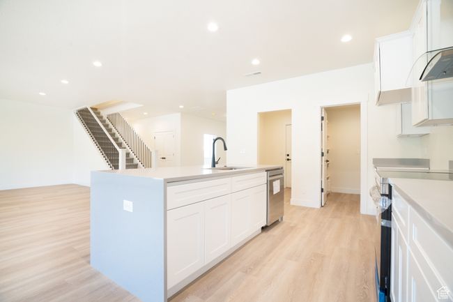 Kitchen featuring appliances with stainless steel finishes, a kitchen island with sink, light wood-type flooring, white cabinets, and recessed lighting | Image 4