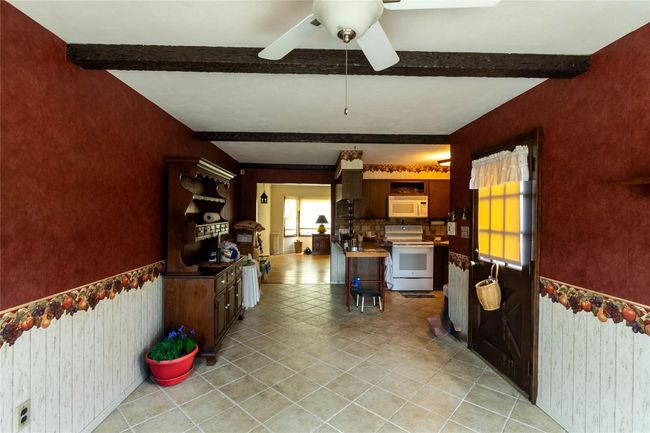 Kitchen with white appliances, light tile patterned flooring, beam ceiling, and a ceiling fan | Image 11