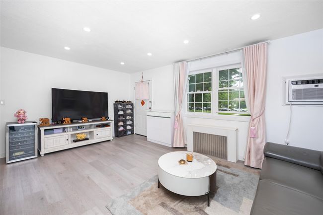 Living room with radiator heating unit, beverage cooler, recessed lighting, an AC wall unit, and light wood finished floors | Image 7
