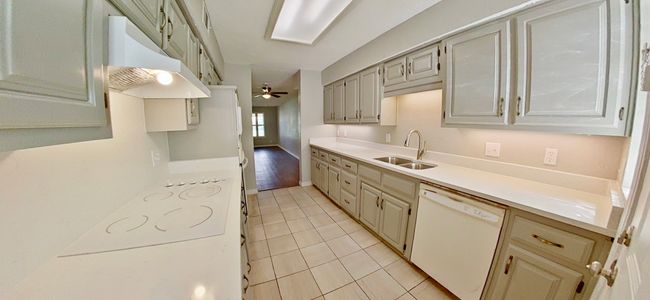 Kitchen with under cabinet range hood, light countertops, dishwasher, light tile patterned floors, and a sink | Image 6