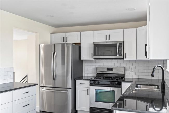 Kitchen with a sink, dark stone countertops, stainless steel appliances, white cabinets, and decorative backsplash | Image 8
