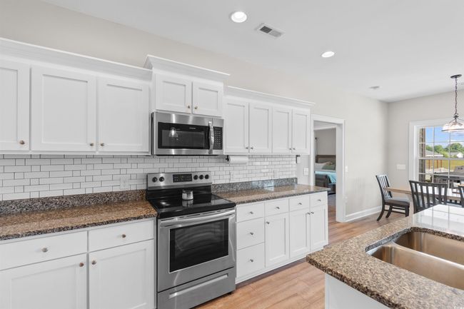 Kitchen with appliances with stainless steel finishes, light wood finished floors, white cabinetry, backsplash, and dark stone countertops | Image 8