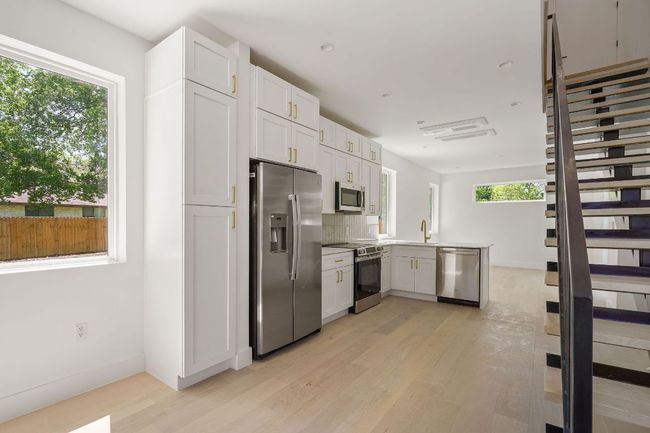 Kitchen with a sink, light wood-type flooring, a peninsula, white cabinetry, and stainless steel appliances | Image 5