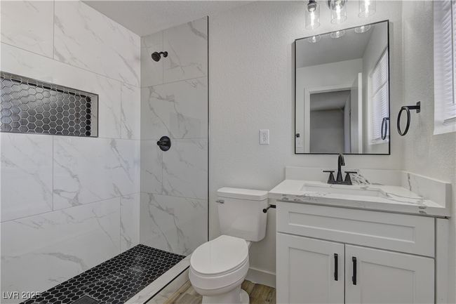 Full bath featuring a tile shower, toilet, vanity, a textured wall, and wood finished floors | Image 20