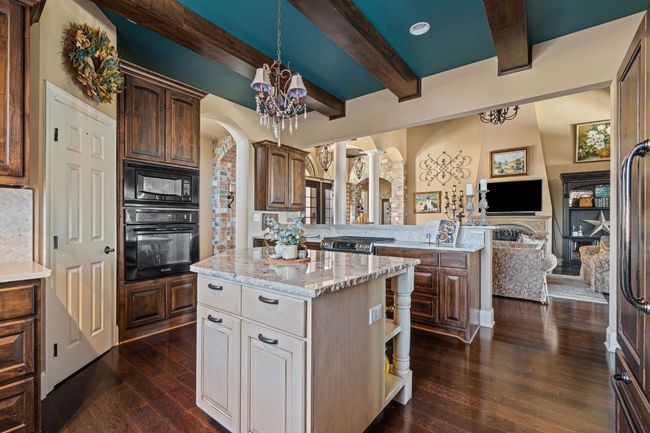 Kitchen with arched walkways, a notable chandelier, beamed ceiling, dark wood-type flooring, and stainless steel appliances | Image 11