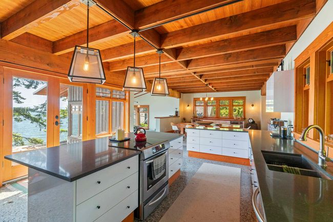 Kitchen with wood ceiling with exposed beams, stainless steel electric stove, white cabinets, dark countertops, and a sink | Image 7
