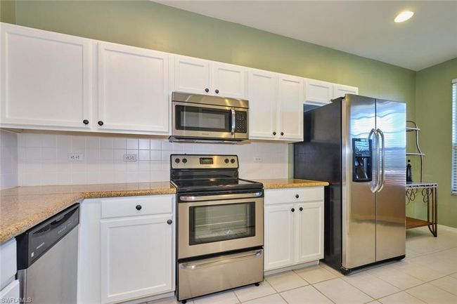 Kitchen featuring tasteful backsplash, white cabinets, stainless steel appliances, light tile patterned flooring, and light stone counters | Image 14
