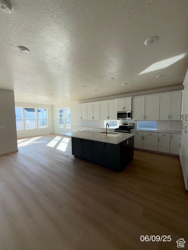 Kitchen with appliances with stainless steel finishes, a sink, wood finished floors, white cabinetry, and a center island with sink | Image 4