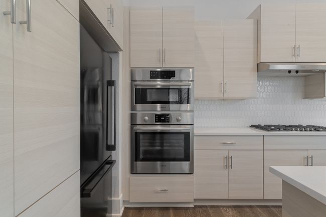 Kitchen with light countertops, backsplash, under cabinet range hood, and stainless steel appliances | Image 14