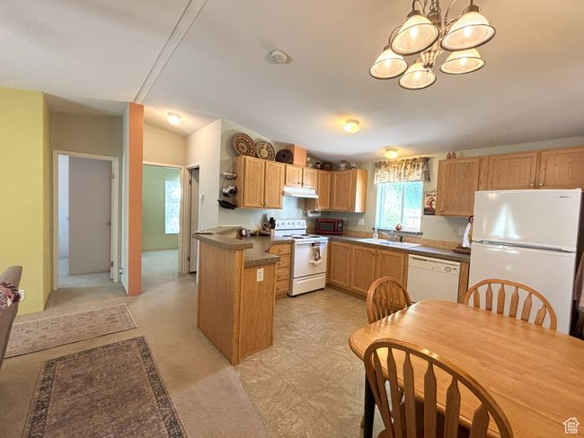 Kitchen featuring white appliances, a sink, a chandelier, under cabinet range hood, and dark countertops | Image 7