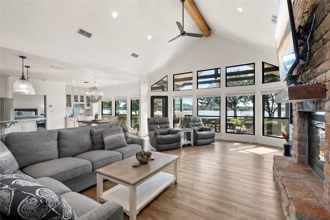 Living area featuring a stone fireplace, beam ceiling, a chandelier, light wood-type flooring, and ceiling fan | Image 13