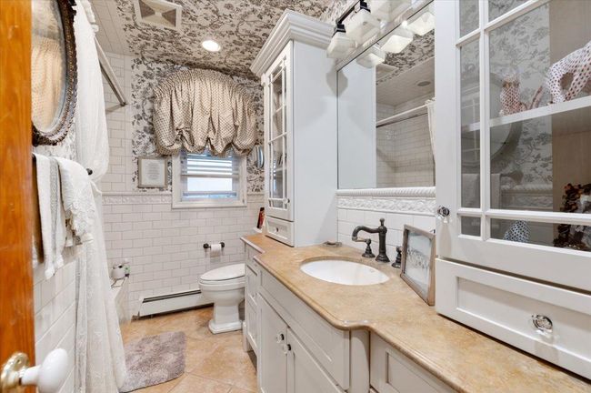 Bathroom with tile walls, tile patterned flooring, vanity, a baseboard heating unit, and toilet | Image 17