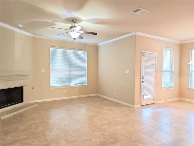 Unfurnished living room with ceiling fan, crown molding, a fireplace with raised hearth, baseboards, and light tile patterned floors | Image 13