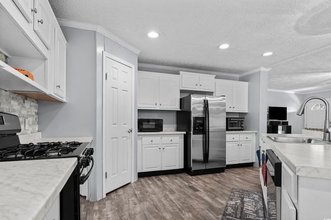 Kitchen with black appliances, a textured ceiling, wood finished floors, ornamental molding, and white cabinetry | Image 19