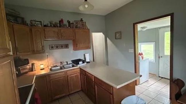 Kitchen with stove, sink, light tile patterned floors, and kitchen peninsula | Image 12