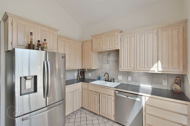 Kitchen with stainless steel appliances, vaulted ceiling, dark countertops, backsplash, and cream cabinets | Image 34