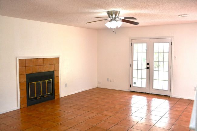 Unfurnished living room with french doors, a tiled fireplace, ceiling fan, a textured ceiling, and tile patterned flooring | Image 5