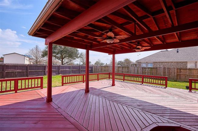 This photo showcases a spacious, covered wooden deck with ceiling fans, ideal for outdoor entertaining. It features a fenced backyard, providing privacy and a great space for relaxation. | Image 46