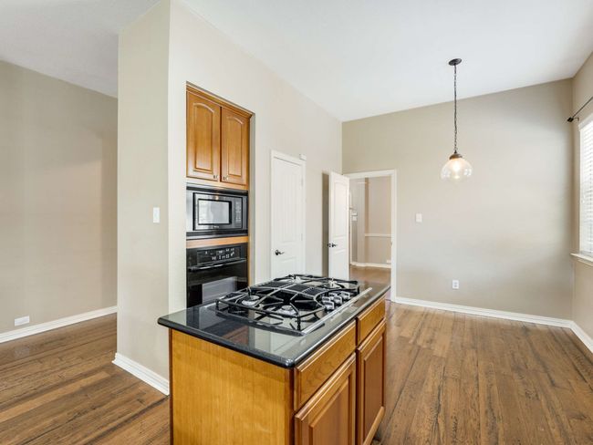 Kitchen with black appliances, dark wood-style flooring, hanging light fixtures, and brown cabinetry | Image 16